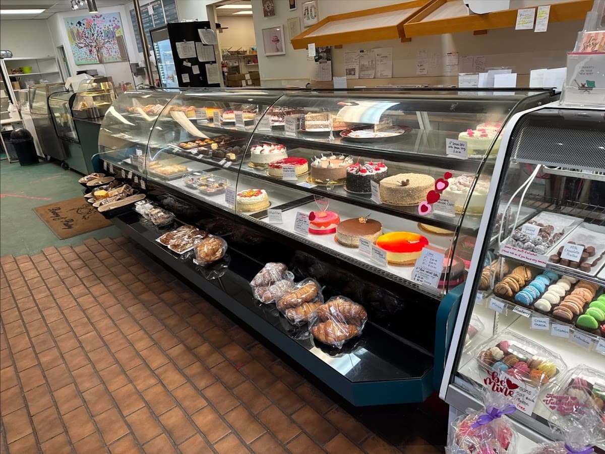 A white bakery tray holds an assortment of pastries, including a sugar doughnut, hot dog bun, and savory pork floss bread in front of a display case.