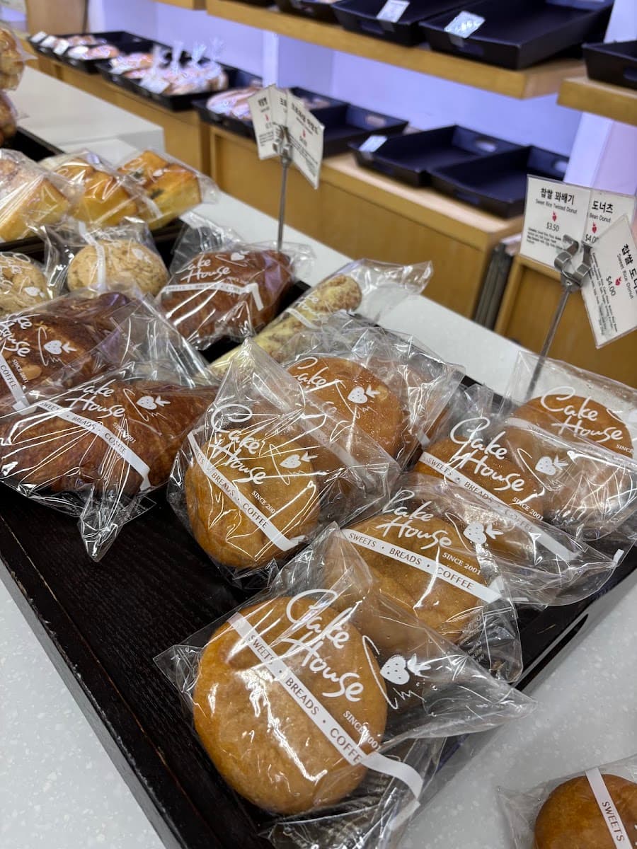 A white bakery tray holds an assortment of pastries, including a sugar doughnut, hot dog bun, and savory pork floss bread in front of a display case.